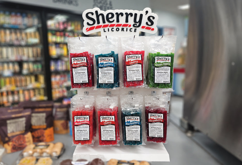 bags of Sherry's Licorice candy displayed on a stand inside a convivence store. The bags contain red, blue, and green licorice, with the Sherry's Licorice logo clearly visible on each package and the main sign above.